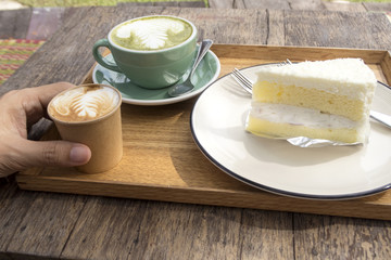 Coconut cake and hot matcha green tea latte and coffee on wooden table.