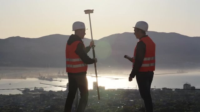 Two surveyor in helmets performing geodesic measurements on top of the mountain