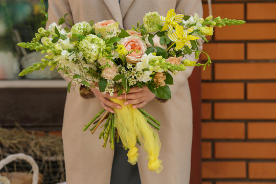Woman holding beautiful blooming bouquet of flowers near shop