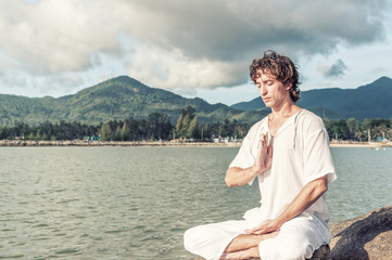 Young man doing pranayama practice on the beach