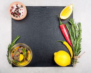 Herbs and spices background. Rosemary, lemon, live oil, salt and pepper on dark slate top view. Copy space for your recipe