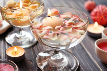 Beautiful spa composition of flower petals with water in bowl and candles on wooden table
