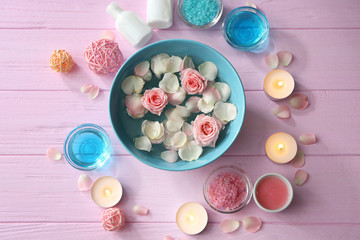 Beautiful spa composition of flower petals with water in bowl and candles on wooden background