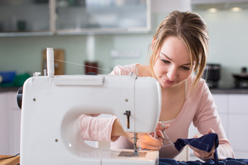 Beautiful young woman sewing clothes with sewing machine (color toned image; shallow DOF) - obrazy, fototapety, plakaty