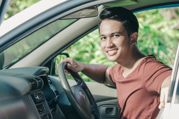 asian man in casual driving a car and looking at camera