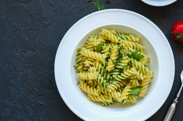 Top view of pasta pesto sauce served in a white plate on a black slate background. Copy space.