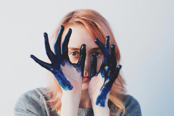 Ginger hair girl look through painted blue fingers