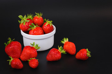 Organic fresh strawberries fruit in white cup on black background