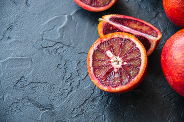 Whole and slices of blood oranges on a black slate background. Copy space and close up.