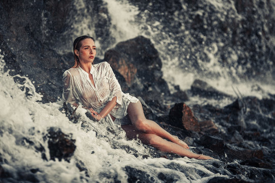 Young woman in white shirt and bikini lies on rock in water flow