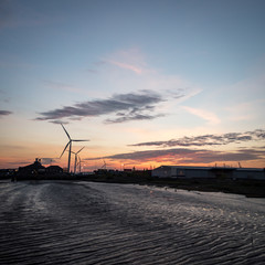 Dusk at the Port of Tilbury, Essex, UK. Sunset view of the low tide of the River Thames and wind turbines turning in the background.