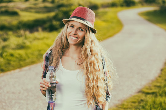 Beautiful young woman drinking water while resting from walking at the country road.
