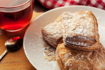 Puff pastries with cup of red fruit tea on a wooden table, selective focus