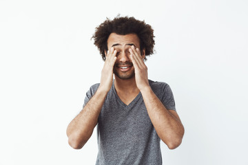 Bored tired african man touching face with hands over white background.