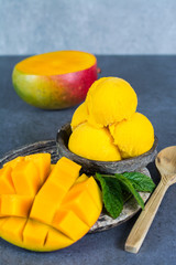 Mango ice cream sorbet with mint leaves and mango fruit in black stone bowl on grey textured backgund