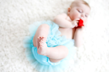 Close-up of legs and feet of baby girl on white background wearing turquoise tutu skirt.