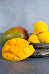 Mango ice cream sorbet with mint leaves and mango fruit in black stone bowl on grey textured...