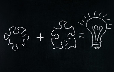 Businessmans Hand drawing puzzle on blackboard to explain business concept. Solving puzzle together. Drawing light bulb on blackboard. Combining the wisdom for developing new idea.