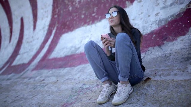 Cute young brunette woman in glasses using smartphone in half pipe 