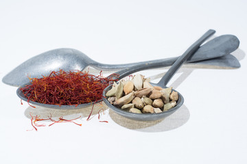 Raw Organic Red Saffron and Cardamom Spices in old tin spoons on white  background
