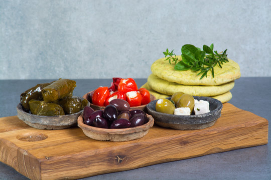 Mediterranean appetizer antipasti tapas bowls with green and calamata olives, feta cheese, stuffed pepper with garlic pita bread, herbs on wooden plank