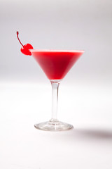 Red drink in martini glass, garnished with marachino cherry. on white background