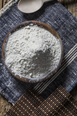 Flour in a wooden bowl, paper bag and spoon. Top view, space for text.