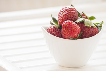 Juicy fresh strawberries in a white bowl on a rough cloth background