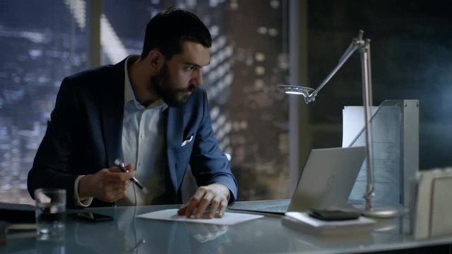 Late at Night Businessman Works on a Laptop and Signs Documents in His Private Office with Big City Window View. Shot on RED EPIC-W 8K Helium Cinema Camera.