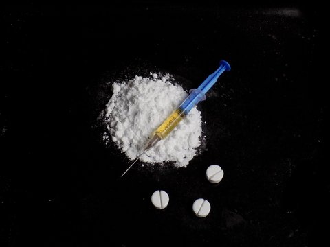 Injection syringe on cocaine drug powder, pills on black background