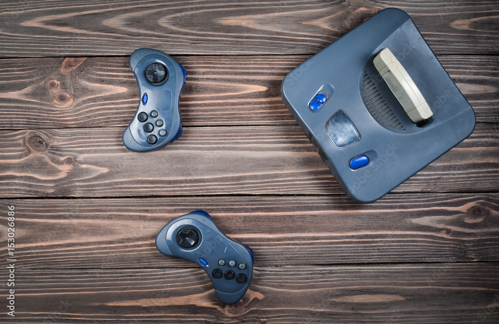 Wall mural game console with a cartridge and joysticks on a wooden table. top view.