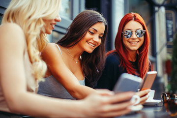 Three beautiful young woman using smartphone in cafe