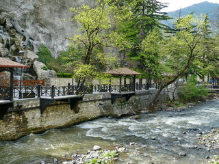 Fototapeta premium Alcove over a mountain stream among rocks and green trees. Mountain stream near the rocks