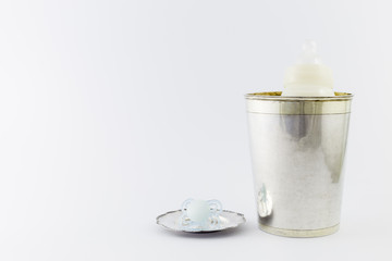 Baby boy luxurious items collection isolated on white background. A milk bottle in a silver champagne bucket and a pacifier on a silver plate.