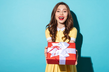 Cheerful pretty girl in dress giving present box to camera