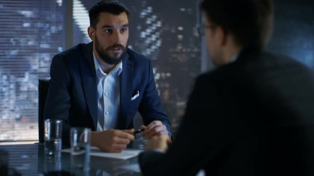 Late at Night Businessman Businessman Has Conversation with Important Client. In the Background Big City Window View. Shot on RED EPIC-W 8K Helium Cinema Camera.