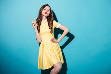 Pretty playful girl in dress showing peace gesture and winking