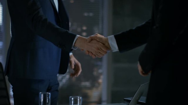 Late at Night Businessman Businessman Has Conversation with Important Client, They Come to an Agreement, Sign Contract and Shake Hands. In the Background Big City Window View. RED Cinema Camera.