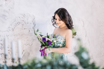 beautiful brunette girl in the open turquoise dress in Studio on white gray background with wedding bouquet looks at them the horizontal copyspace