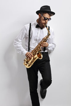 Jazz musician leaning against a wall and playing saxophone