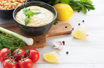 Bowl with hummus, chickpeas, lemon, cherry tomatoes and herbs on a white rustic wooden background.
Middle Eastern cuisine. Background hummus with place for text.