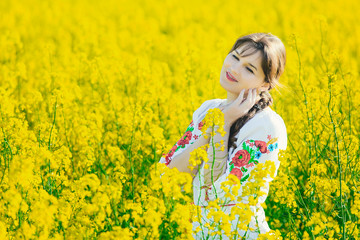 Beautiful young woman in Ukrainian embroidered standing in a field of yellow rape flowers