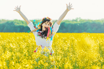 Naklejka na ściany i meble Beautiful young woman in Ukrainian embroidered standing in a field of yellow rape flowers