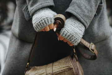 A girl in a coat and knitted gloves is holding a leather bag. Close-up of hands. A woman expects, nervous. Compressed hands, beautiful manicure