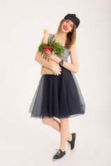 Young french girl holding grocery shopping bag with vegetables. Cute girl in a cap buying food isolated