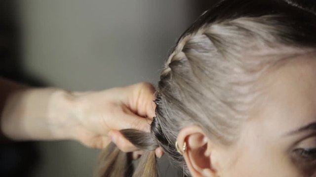 Hairdresser plaiting braids for young brunette woman. Professional styling makes styling easier