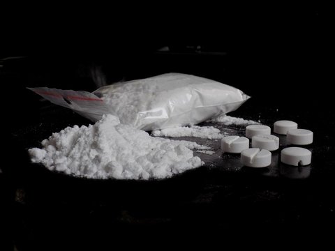 Cocaine drug powder bag and pile and pills on black background