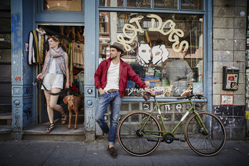 Germany, Hamburg, St. Pauli, Man with bicycle waiting in front of vintage shop, woman with dog coming out