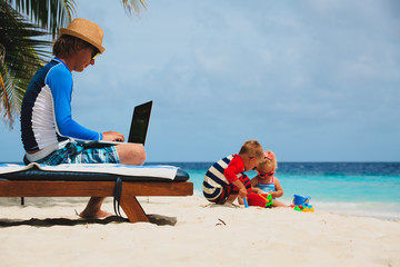 father working on laptop while kids play at beach