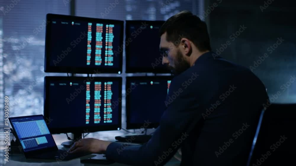 Poster Late at Night Trader Reads Number on His Multiple Displays with Stock Information on Them. In Background Big City Window View. Shot on RED EPIC-W 8K Helium Cinema Camera.
